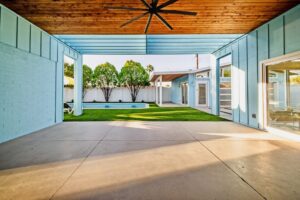 Renovated Mariposa mid-century home in Scottsdale featuring a covered patio with wood ceiling, blue exterior siding, large glass doors, and backyard swimming pool.