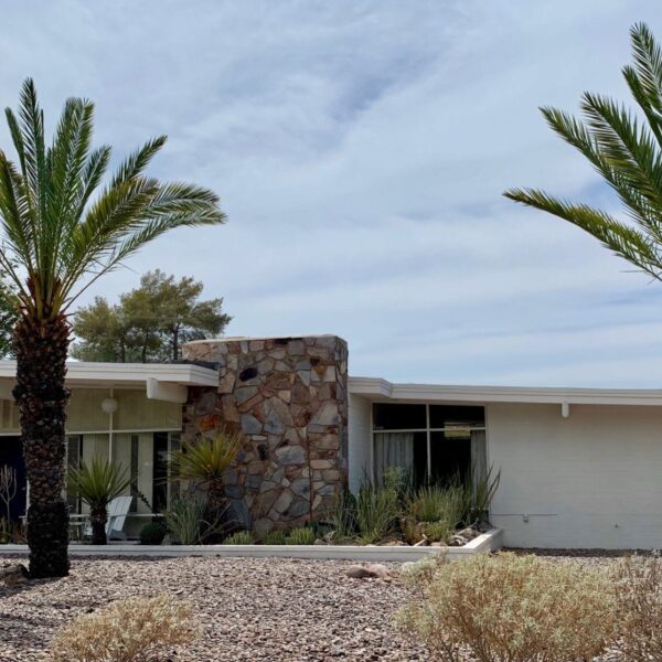 Mid-century modern home in Marion Estates Phoenix with stone chimney, low roofline, palm trees, desert landscaping, and broad front windows.