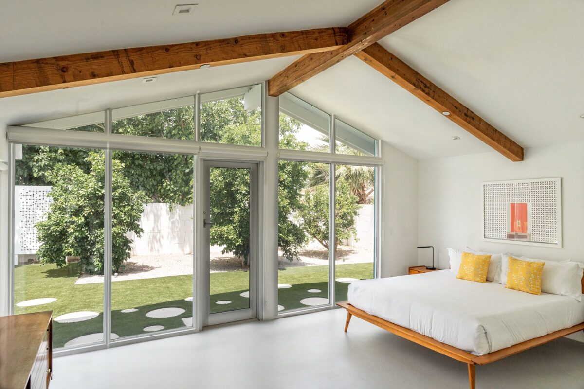 Mid-century modern bedroom with vaulted ceiling, exposed wood beams, glass wall, and indoor-outdoor connection.