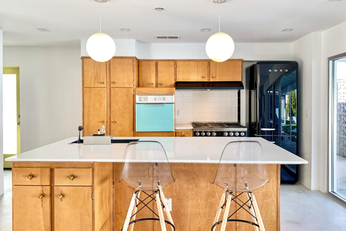 Renovated open-concept kitchen and family room at the Sheridan House featuring restored wood cabinetry, white quartz countertops, modern lighting, and backyard views.