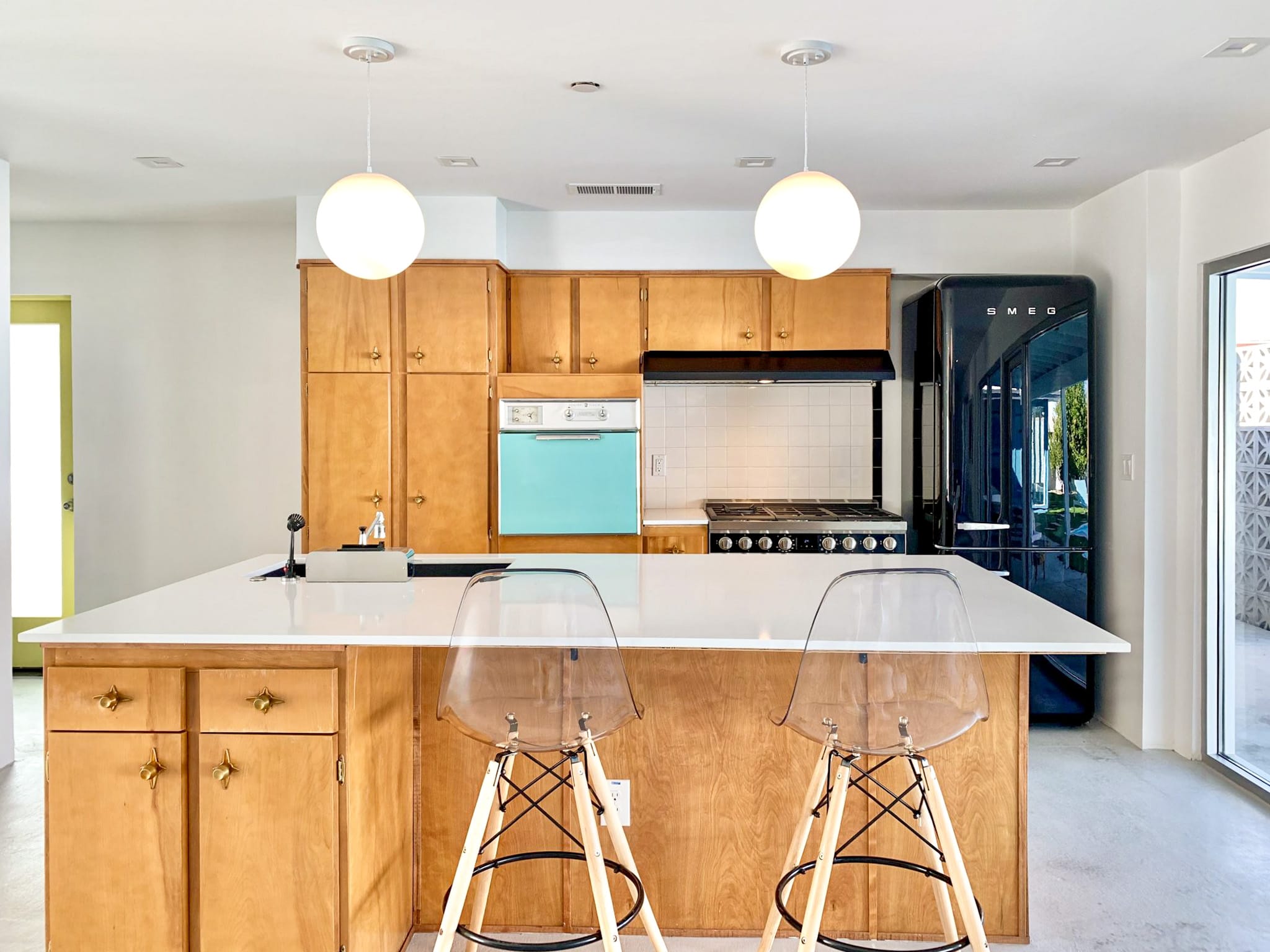 Renovated open-concept kitchen and family room at the Sheridan House featuring restored wood cabinetry, white quartz countertops, modern lighting, and backyard views.