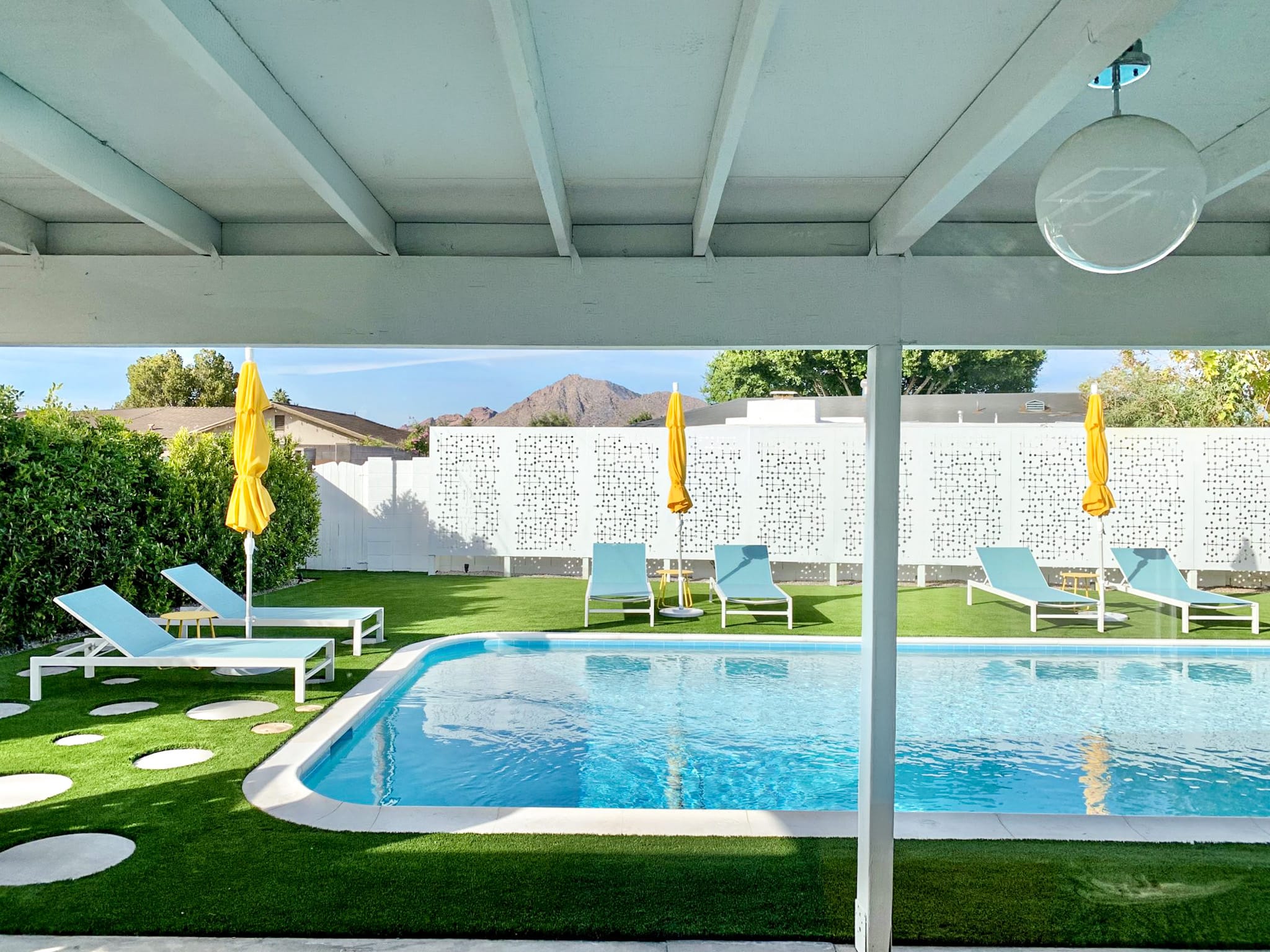 Sheridan rear patio and pool in Scottsdale with covered outdoor living area, breeze block wall, yellow umbrellas, pool, and mid-century modern landscape design.